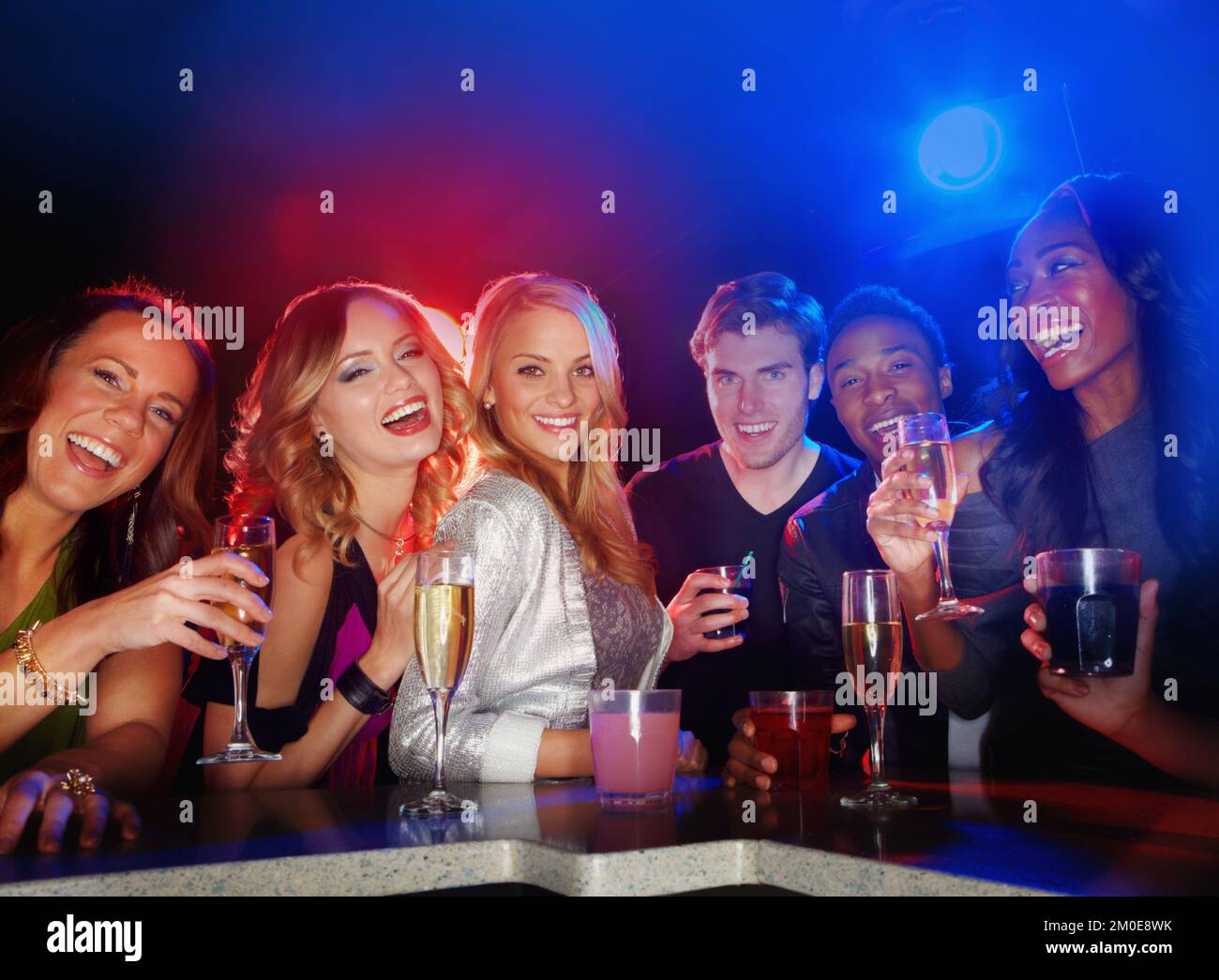 Genießen Sie die Nachtlokale der Stadt. Eine multiethnische Gruppe junger Freunde, die vor der Kamera lächeln, während sie in einem Nachtclub einen Drink genießen. Stockfoto