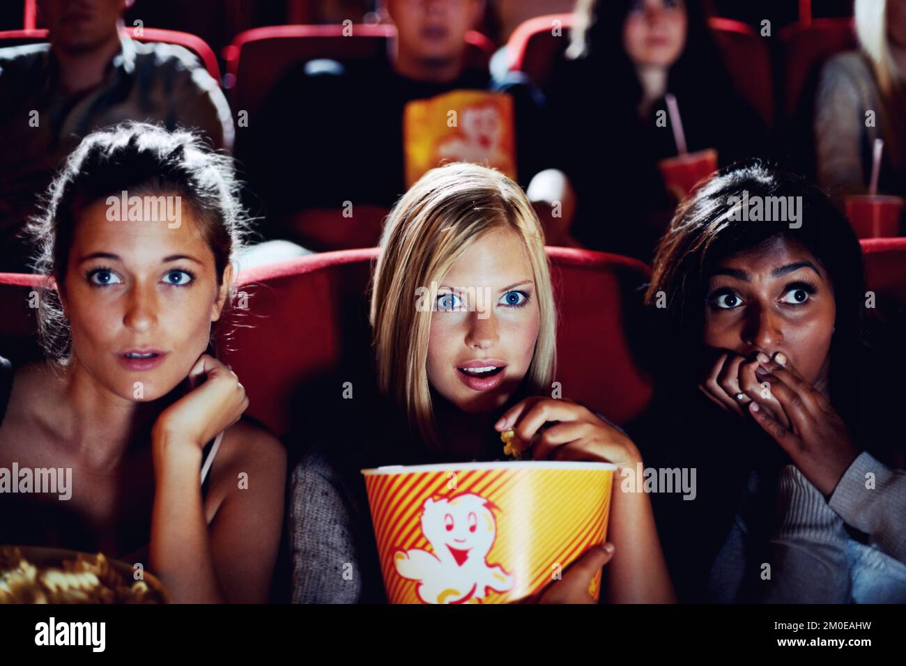 Sie sind wirklich in diesen Film vertieft. Drei Freundinnen sitzen dicht beieinander und sehen verängstigt und nervös in einem Kino aus. Stockfoto