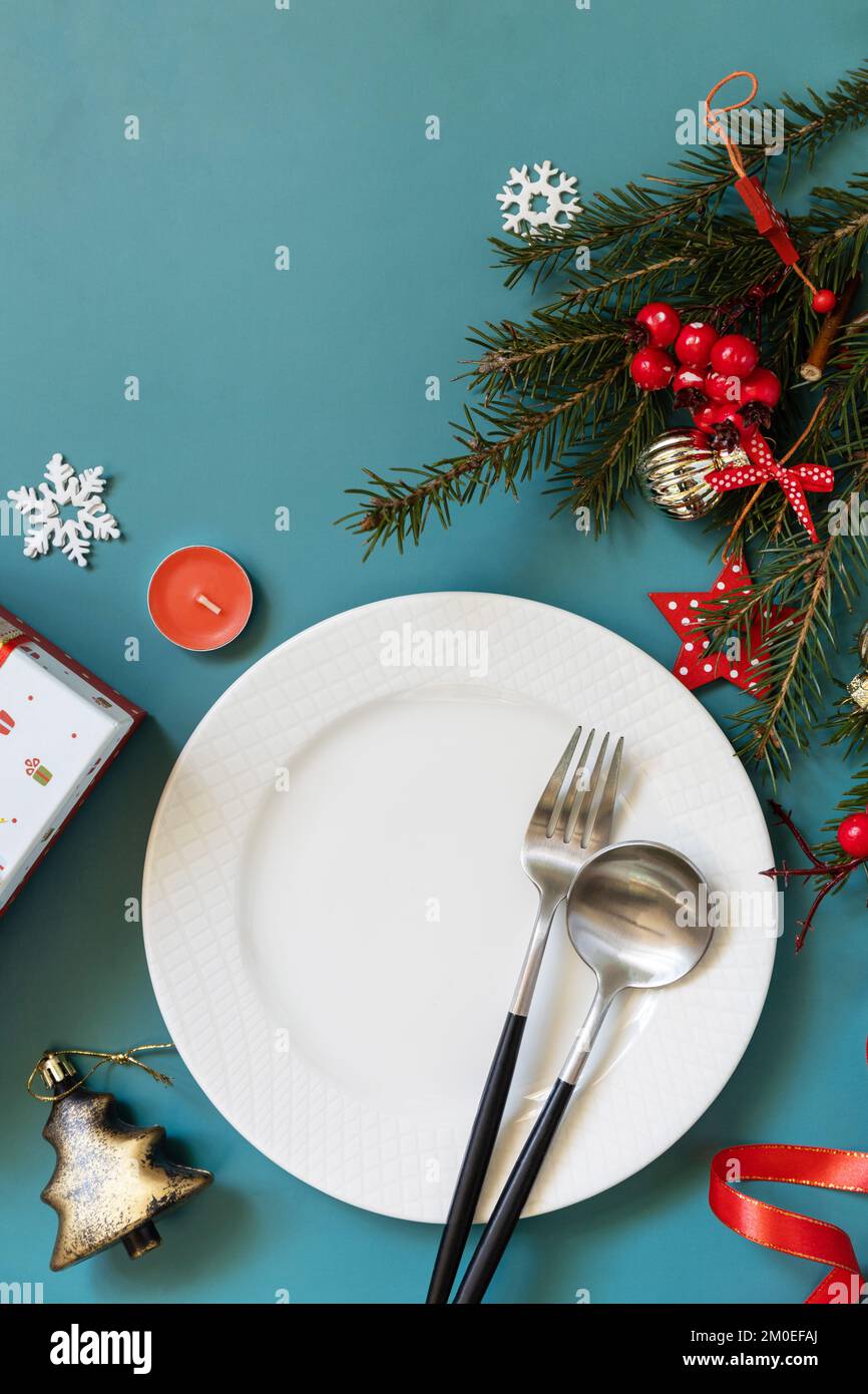 Flach liegender Weihnachtstisch mit Teller, Besteck, Geschenkboxen und weihnachtsdekorationen auf grünem Hintergrund. Stockfoto