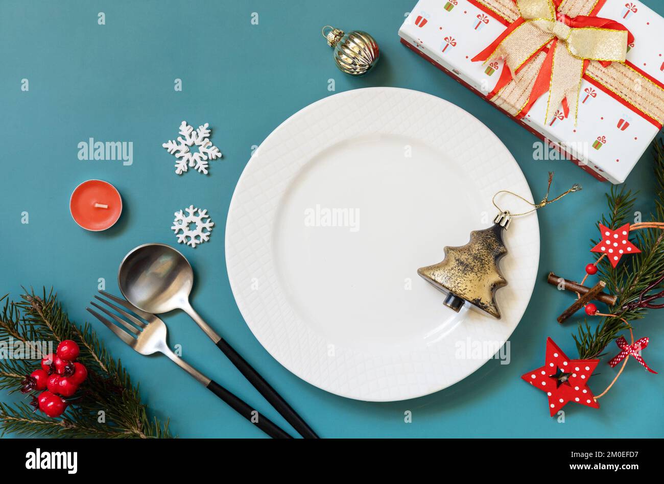 Flach liegender Weihnachtstisch mit Teller, Besteck, Geschenkboxen und weihnachtsdekorationen auf grünem Hintergrund. Speicherplatz kopieren. Stockfoto