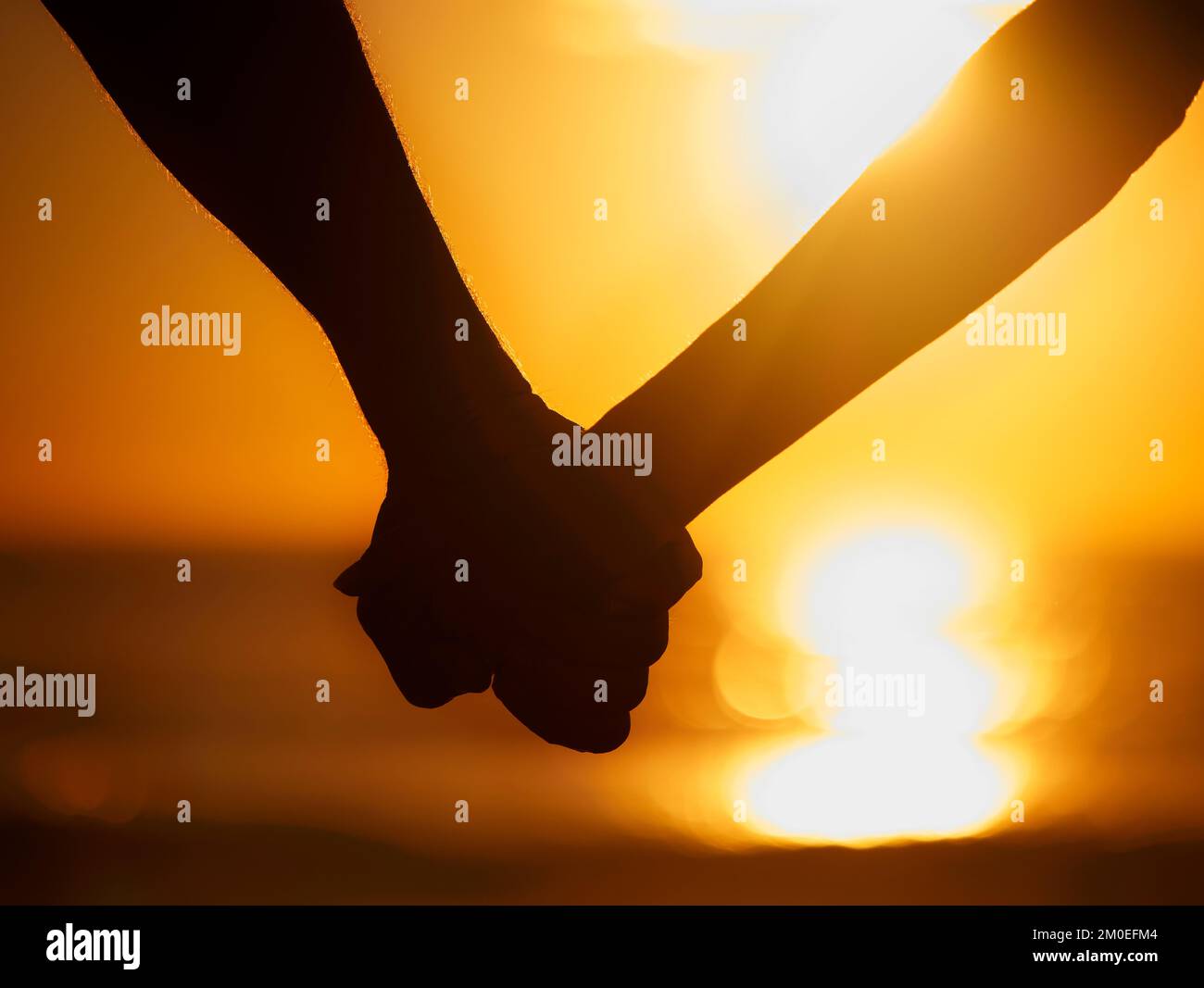 Nahaufnahme eines Silhouettenpaares, das während eines wunderschönen Sonnenuntergangs am Strand Händchen hielt Stockfoto