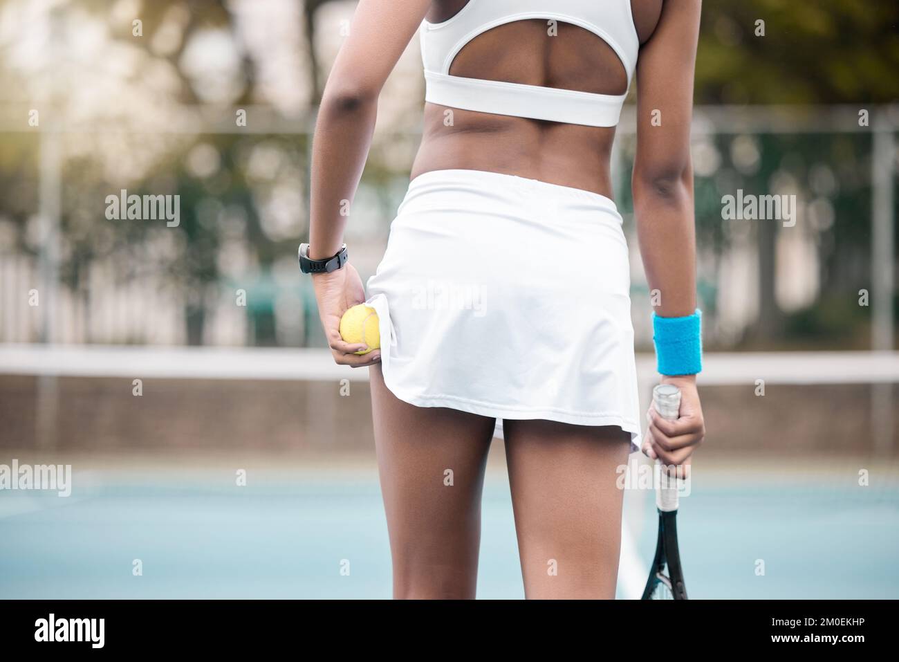 Die Rückseite einer Tennisspielerin, die ihren Schläger auf dem Platz hält. Eine afroamerikanische Tennisspielerin hält ihren Ball und Schläger auf dem Platz. Profi-Tennis Stockfoto