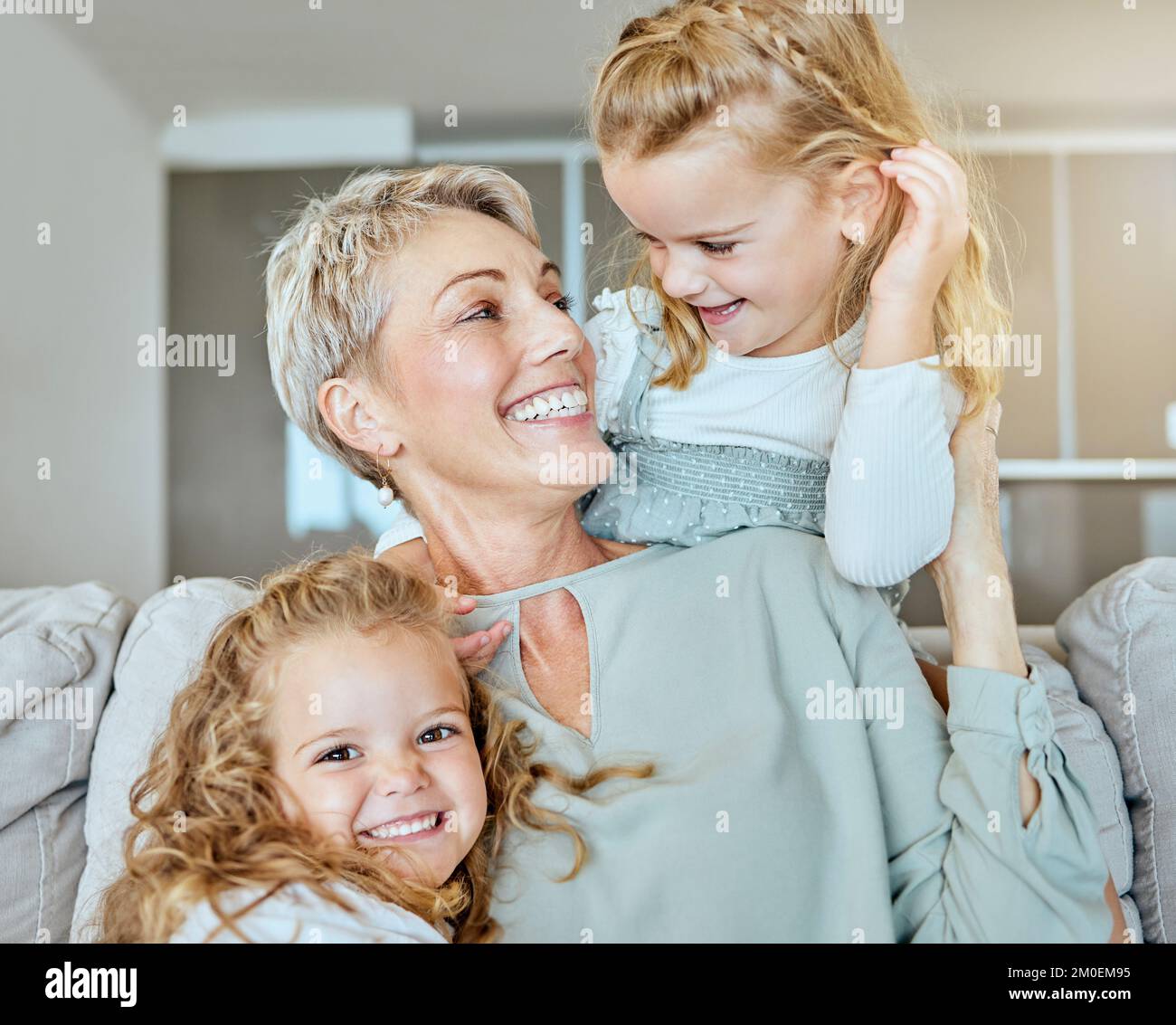 Eine glückliche Familie aus drei Frauen, die sich nur auf dem Sofa entspannen. Lächelnde Oma, die zu Hause auf ihre beiden Enkelinnen aufpasst Stockfoto