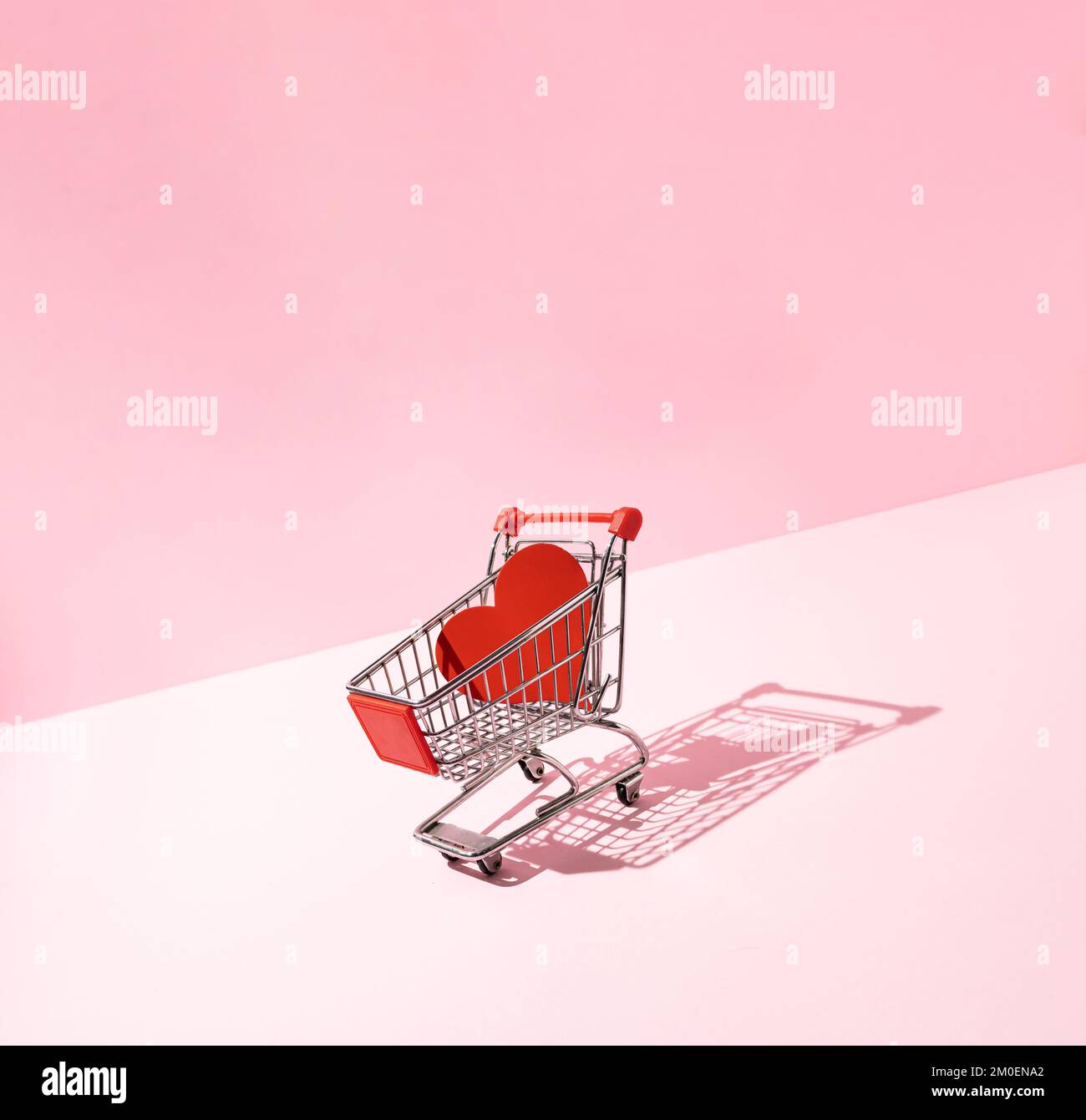 Rotes Herz im Warenkorb auf pinkfarbenem Hintergrund. Kreative Liebe oder Valentinstag-Minimalkonzept. Stockfoto