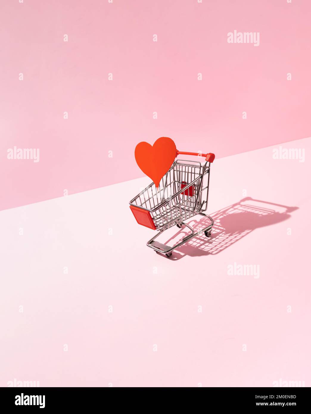 Rotes Herz im Warenkorb auf pinkfarbenem Hintergrund. Kreative Liebe oder Valentinstag-Minimalkonzept. Stockfoto