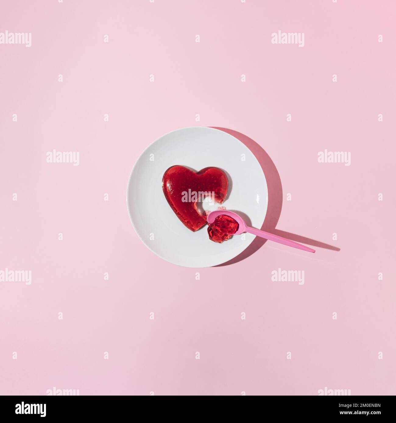 Rotes Gelee-Herz mit Kunststofflöffel auf weißem Teller. Liebe oder Valentinstag Minimalkonzept. Stockfoto