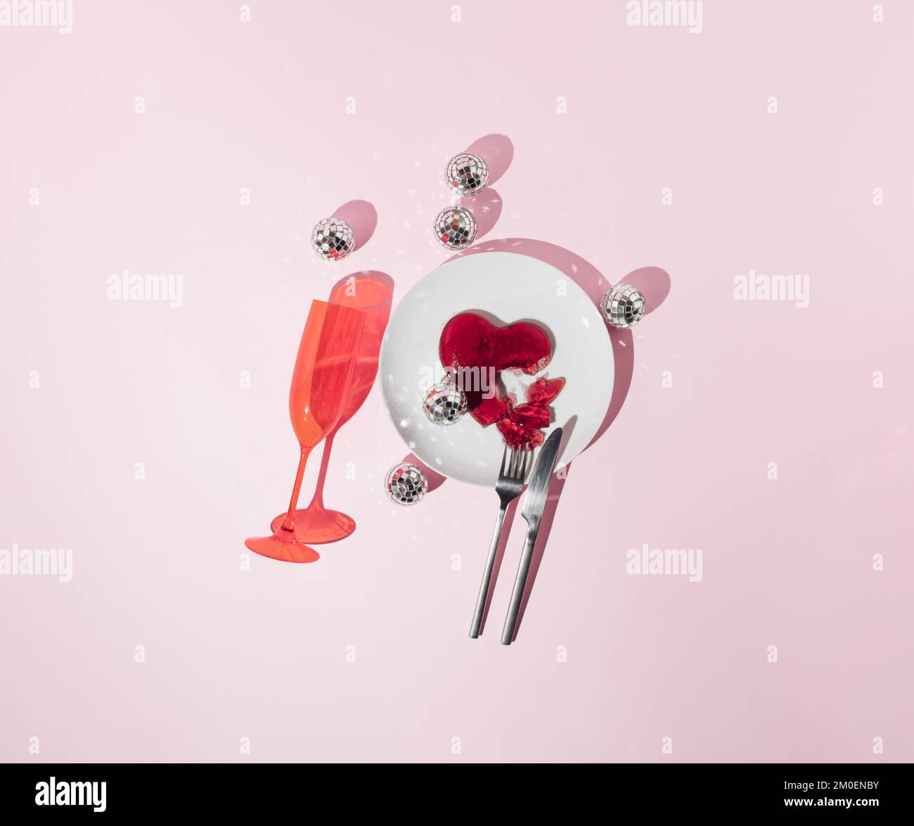 Rotes Gelee-Herz, Discokugeln, Messer und Gabel, Teller und Trinkglas auf pinkfarbenem Hintergrund. Liebe oder Valentinstag Minimalkonzept. Stockfoto