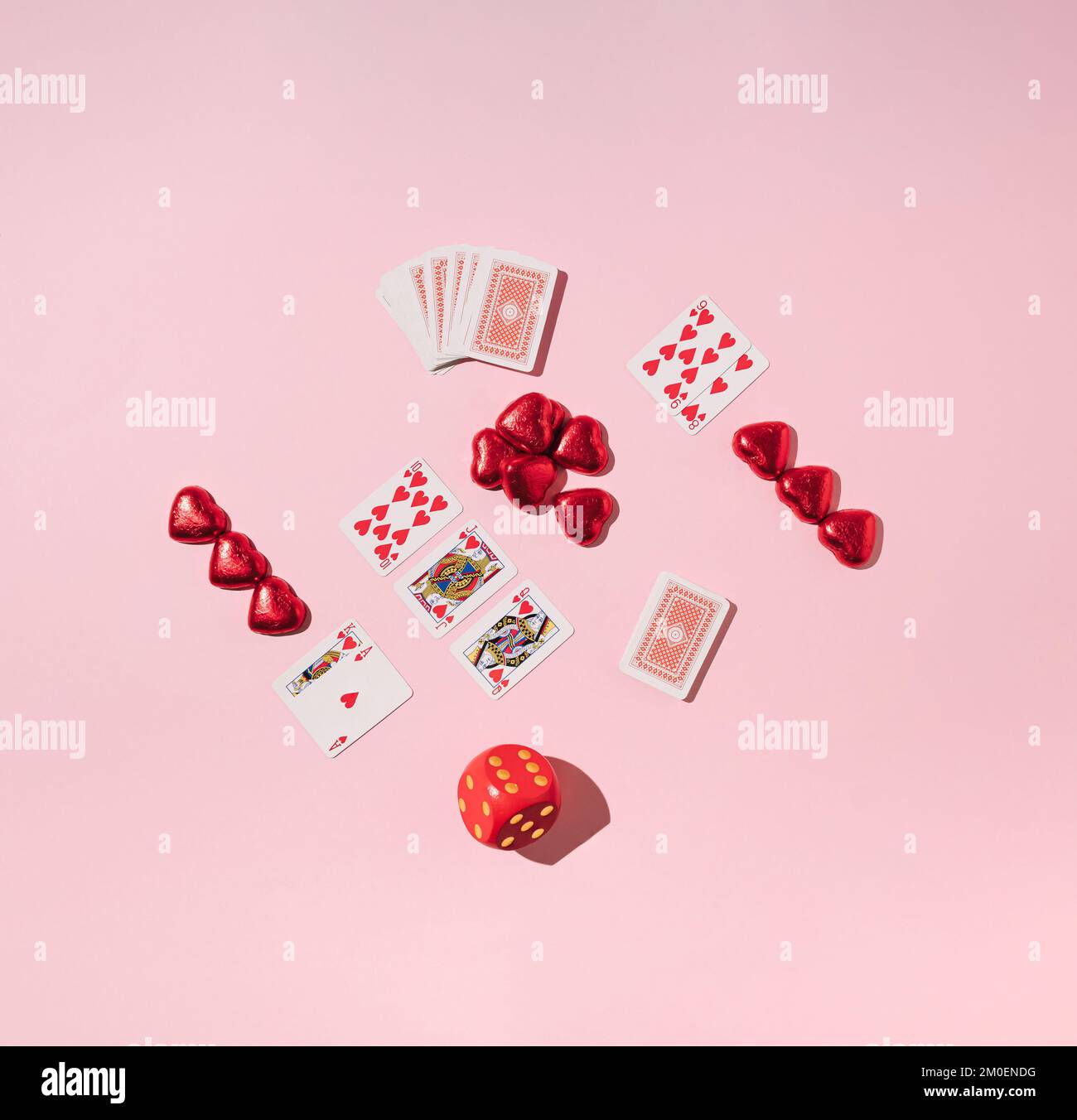 Valentinsspiele. Pokerkarten, Schokoladenherzen und Würfel auf pinkfarbenem Hintergrund. Minimales Liebeskonzept. Stockfoto