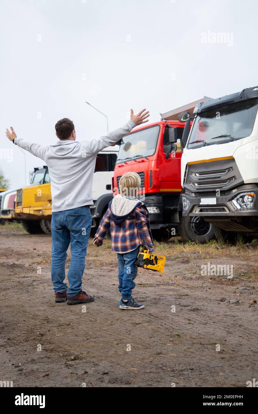 Ein Mann und ein Junge stehen vor großen Lastwagen, Blick von hinten. Sohnes Leidenschaft für Autos, Vater und Kind schauen sich Fahrzeuge auf dem Parkplatz an Stockfoto