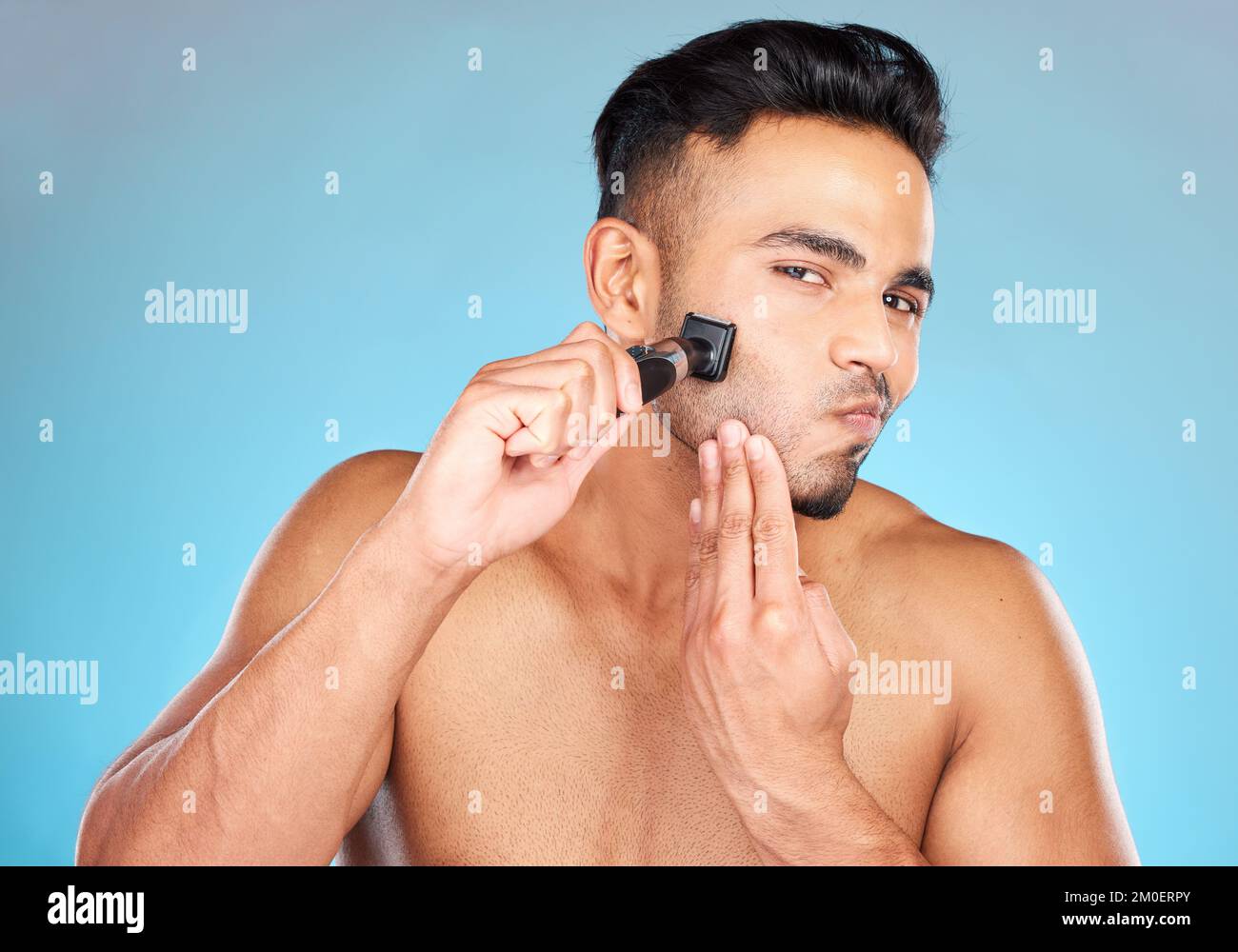 Mann, rasieren und rasieren für Wellness, Hautpflege und Kosmetik vor blauem Studiohintergrund. Indischer Bart und Rasierer für natürliche Schönheit, sanfte und Stockfoto