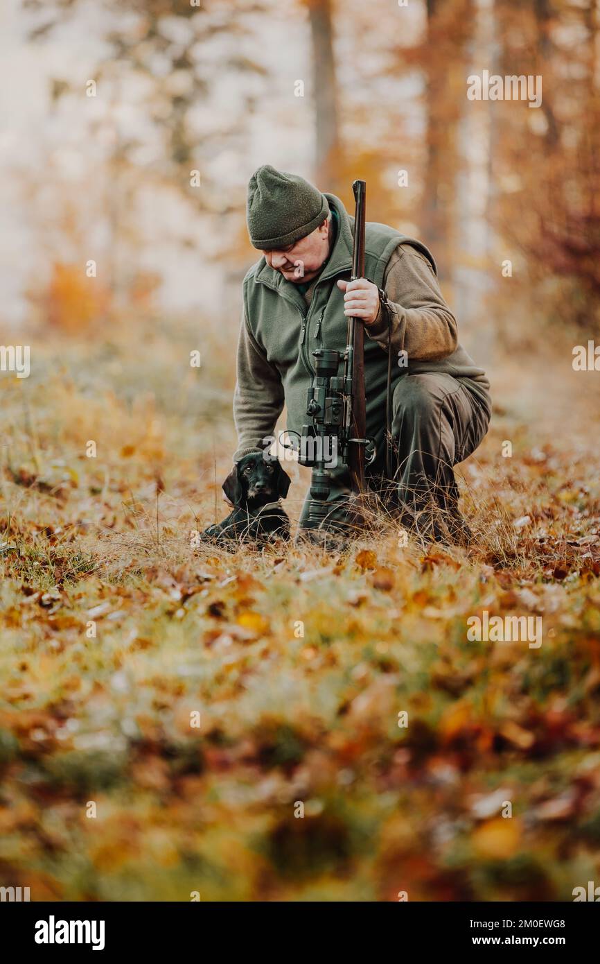 Jäger oder Ranger mit Waffe oder Gewehr mit einem Hund im Wald auf der Jagd nach Wild, Jagdzeit, Herbstsaison, Jagd- und Menschenkonzept Stockfoto