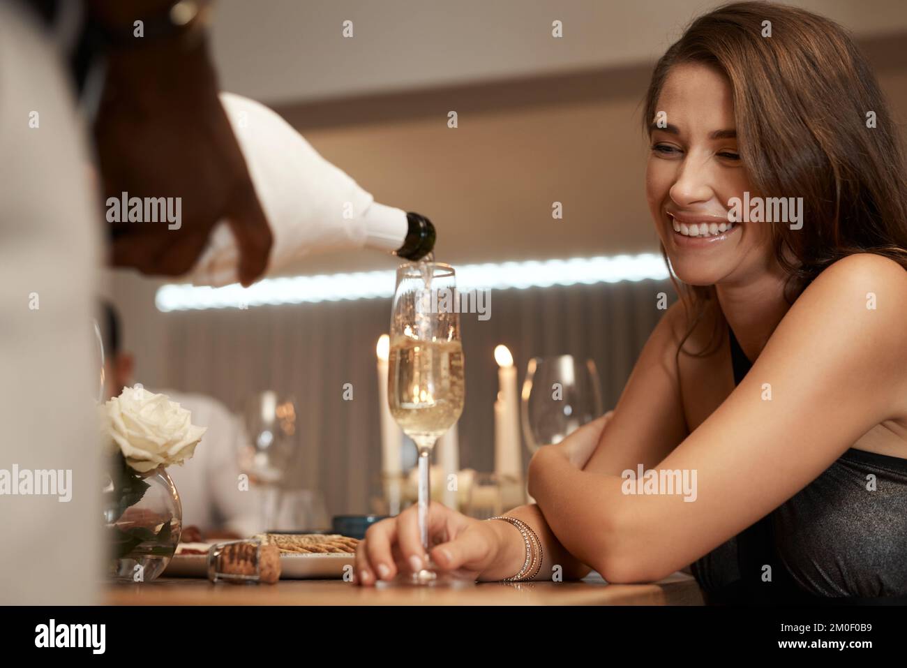 Glückliche Frau, Champagnerglas und Restaurant mit einem Kellner, der Alkohol für eine Feier, Geburtstag oder Neujahrsfeier ausschüttet. Frau mit einem Lächeln am Tisch Stockfoto