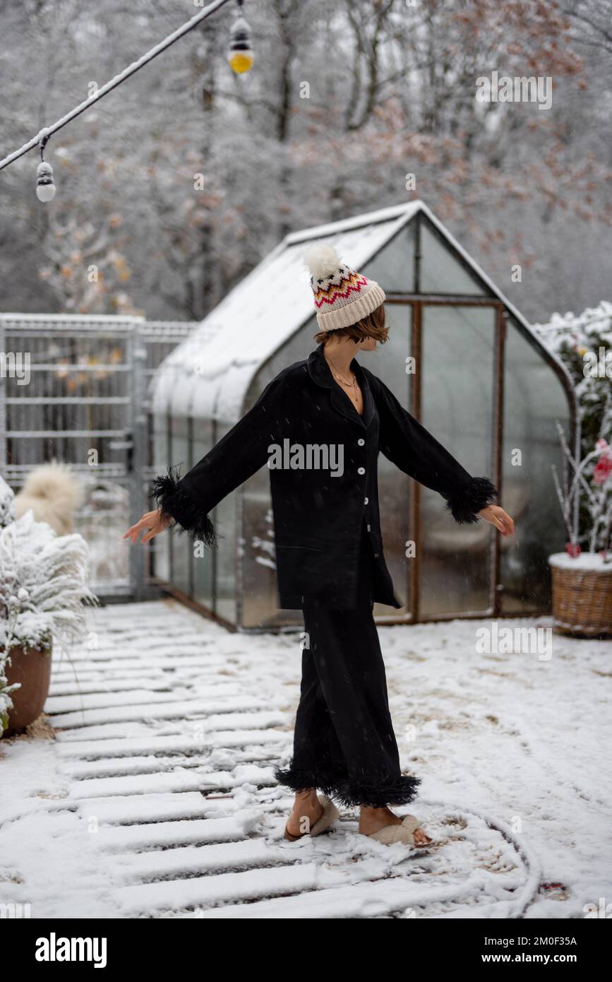 Frau in Schlafkleidung und Hut, die im verschneiten Garten tanzt Stockfoto