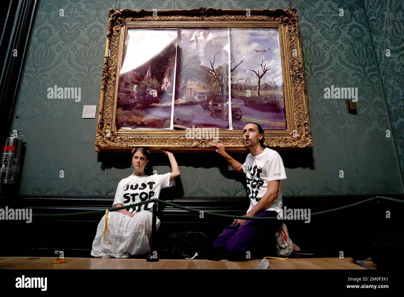 Aktenfoto vom 04.07/22 von Demonstranten der Just Stop Oil Climate Protestgruppe, die ihre Hände an den Rahmen von John Constable's The Hay Wain klebten, nachdem sie das Gemälde zuerst mit ihrem eigenen Bild in der National Gallery, London, bedeckt hatten. Hannah Hunt und Eden Lazarus sind am Westminster Magistrates' Court erschienen, angeklagt, das Hay Wain Gemälde und den Rahmen in der National Gallery kriminell beschädigt zu haben. Ausgabedatum: Dienstag, 6. Dezember 2022. Stockfoto