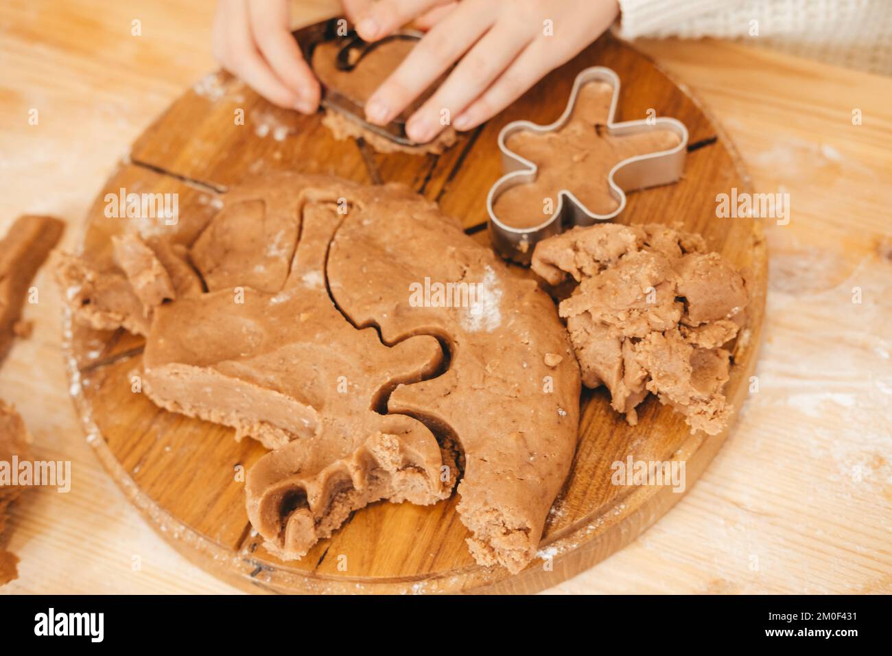 Kinderhände schnitzen Kekse auf Lebkuchenteig aus Figuren. Mädchen bereitet weihnachtskekse auf einem Holztisch zu Stockfoto