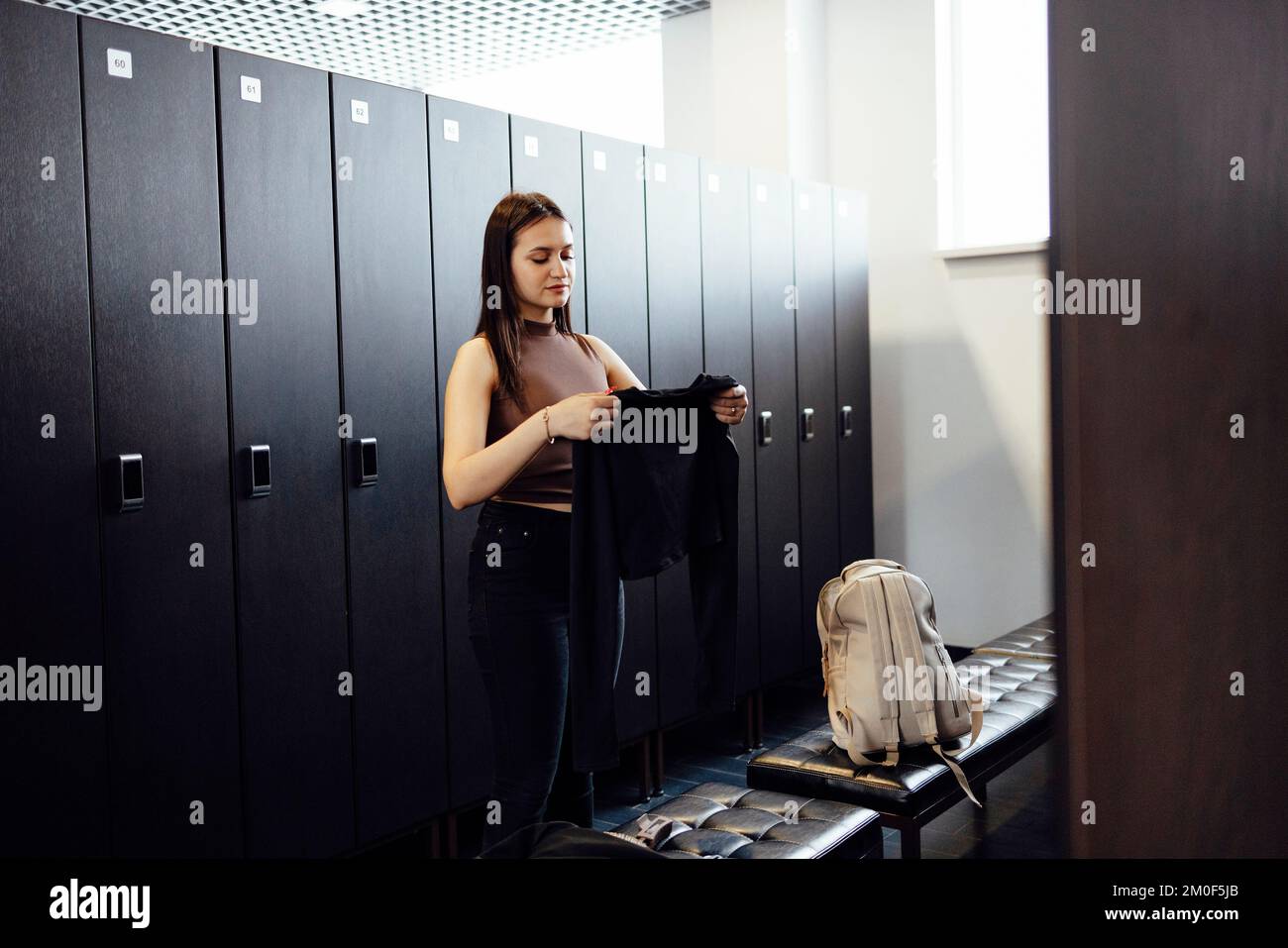 Wunderschön sitzende junge brünette Frau mit Sportkleidung in der Umkleidekabine des Fitnessstudios, die sich auf das Training vorbereitet Stockfoto