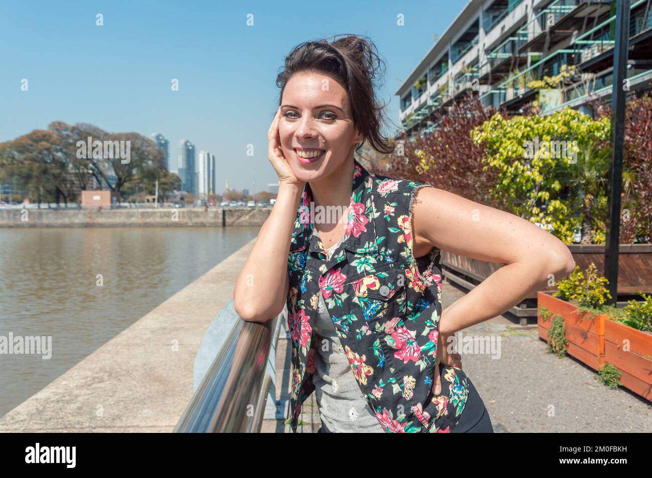 Wunderschöne weiße Erwachsene Touristin, lehnt sich auf ein Geländer vor dem Deich in puerto madero argentinien, schaut in die Kamera und lächelt, das Leben Stockfoto