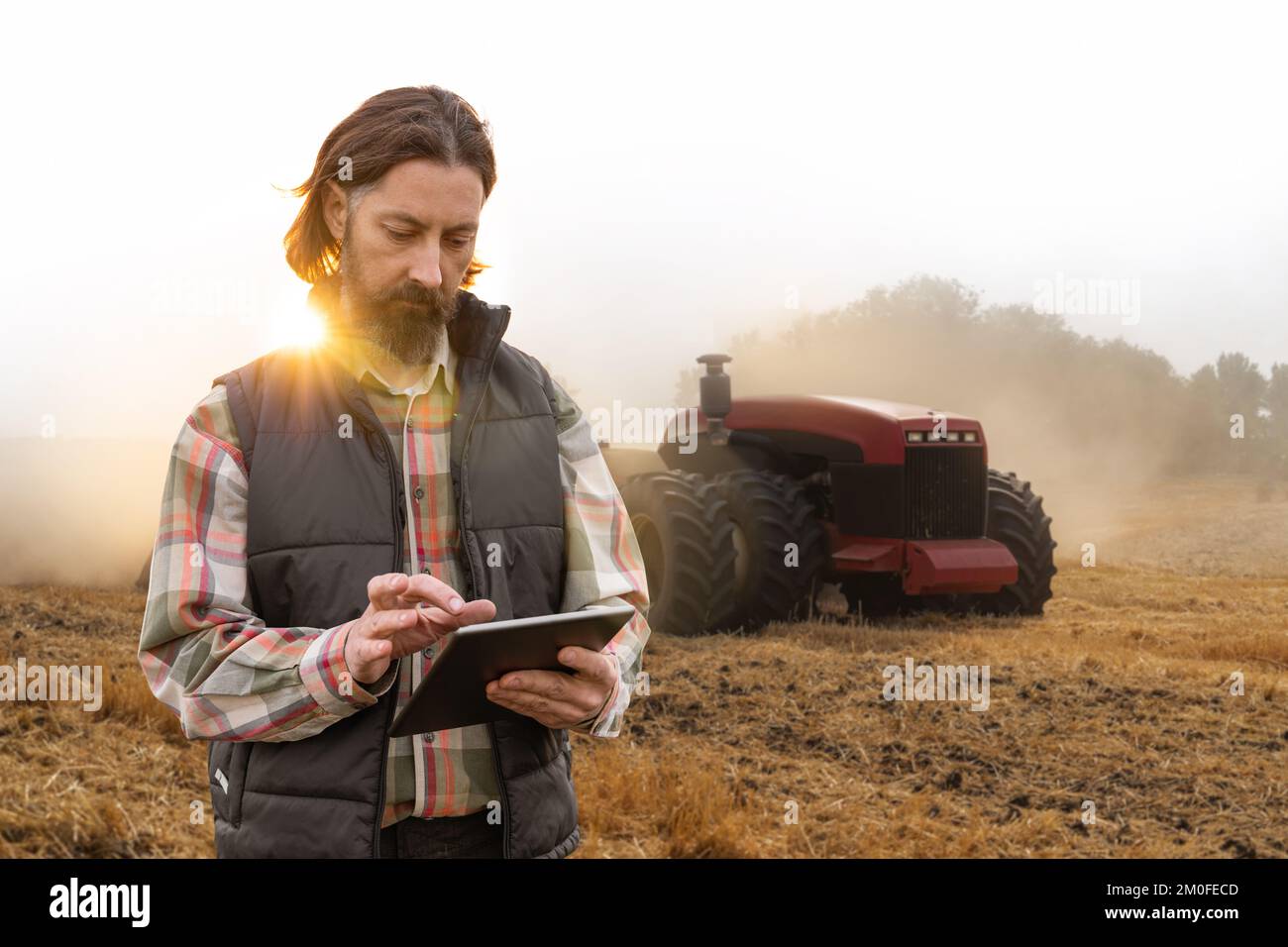 Ein Landwirt mit einem digitalen Tablet steuert einen autonomen Traktor auf einem intelligenten Betrieb Stockfoto
