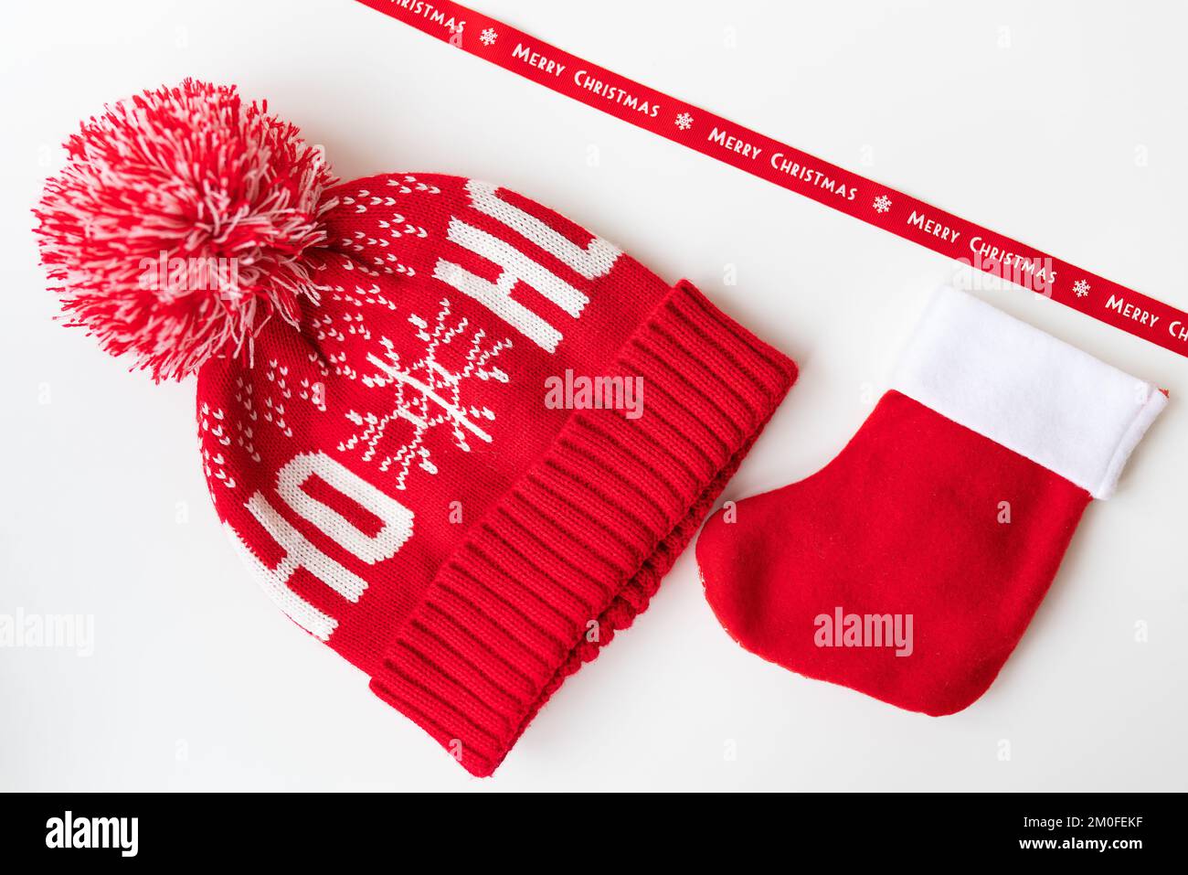 Rotes Band mit Aufschrift Frohe Weihnachten mit rotem Hut, Fäustlingen und roter Socke auf weißem Tisch. Das Konzept der Neujahrsfeier und Stockfoto