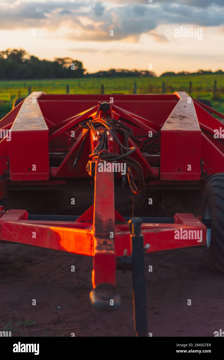 Ein vertikaler Schuss eines roten Traktors auf einem Ackerfeld bei Sonnenuntergang Stockfoto