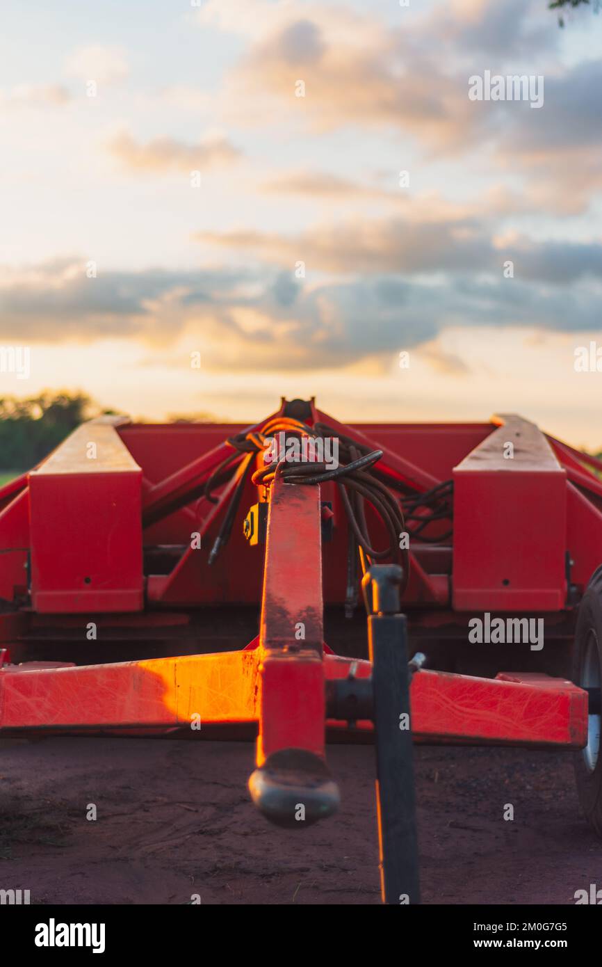 Ein vertikaler Schuss eines roten Traktors auf einem Ackerfeld bei Sonnenuntergang Stockfoto
