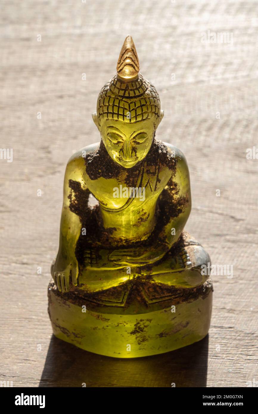 Wunderschöne buddha-Statue aus gelbem grünen Kristall mit Hintergrundbeleuchtung auf hellem Holzhintergrund Stockfoto