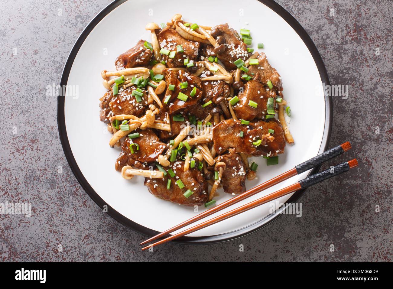 Japanische Küche, gebratenes Rindfleisch mit Buche-Pilzen in Teriyaki-Sauce mit grünen Zwiebeln und Sesam, Nahaufnahme auf einem Teller auf dem Tisch. Horizontal oben Stockfoto