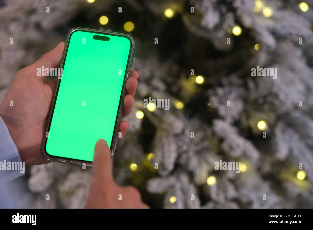 Nahaufnahme Hand, die nachts neben dem Weihnachtsbaum auf ein Smartphone mit grünem Bildschirm tippt Stockfoto