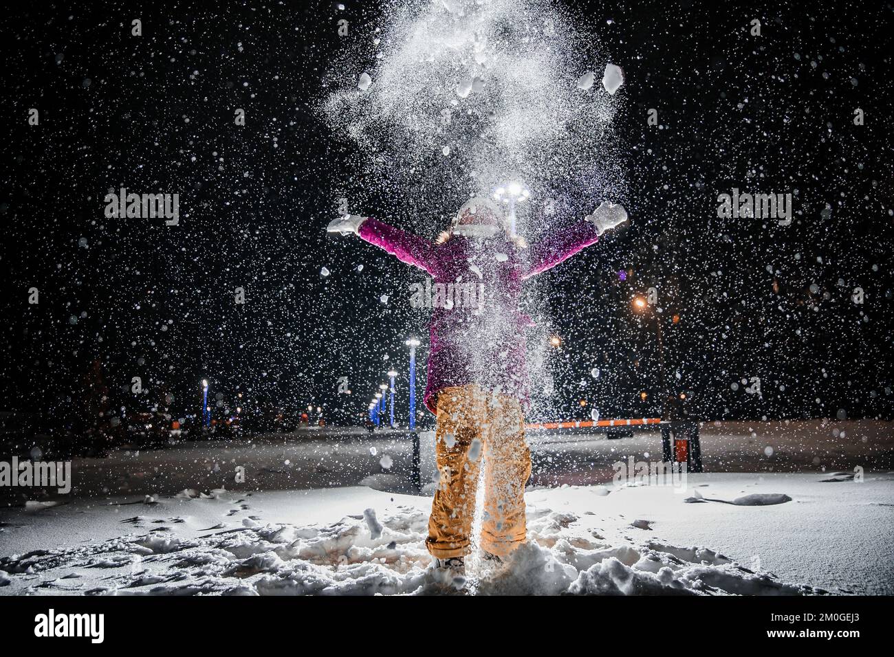 Ein kleines Mädchen ist sehr glücklich mit dem ersten Schnee in einer kalten Winternacht. Realistische, natürliche Schneeflocken auf schwarzem Hintergrund. Stockfoto