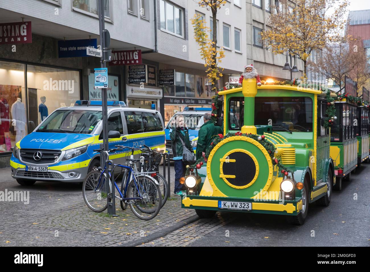 Der Kölner Minizug steht in der Altstadt neben Polizeiautos, Köln, Deutschland. Die Koelner Bimmelbahn für Stadtrundfahrten steht in Stockfoto