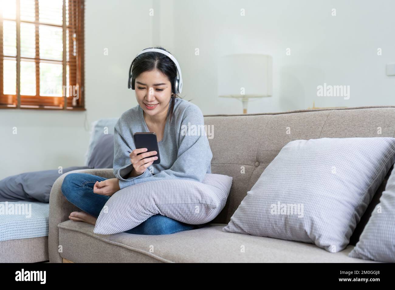 Asiatische Frauen hören Musik mit Mobiltelefon und Kopfhörern. Ein ruhiges Wochenende zu Hause, entspannen Sie sich auf dem Sofa, genießen Sie Ihre Lieblingsmusik, beliebte Musik, nutzen Sie modern Stockfoto