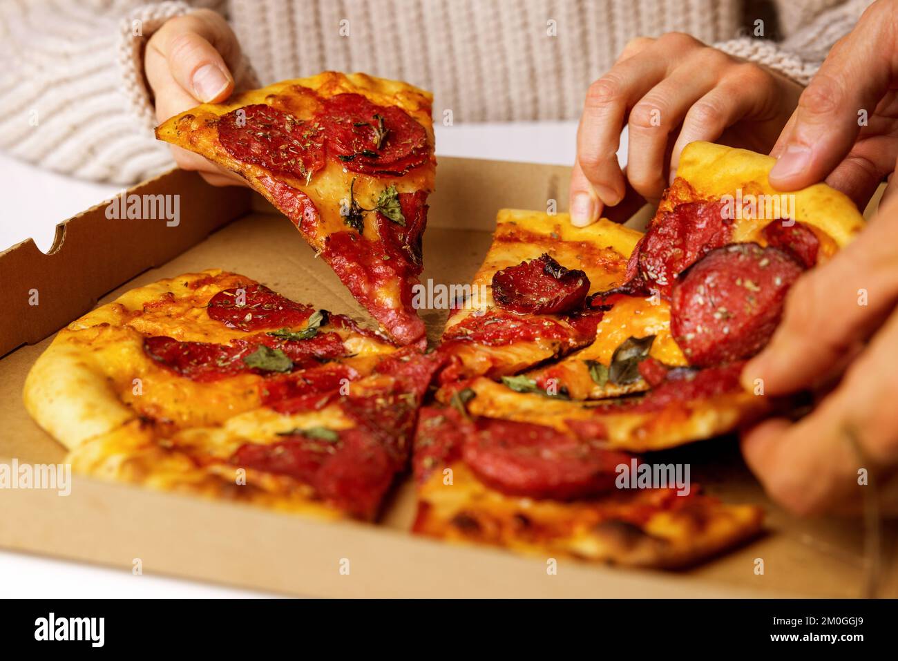 Hände nehmen Peperoni-Pizzastücke aus der Schachtel Stockfoto