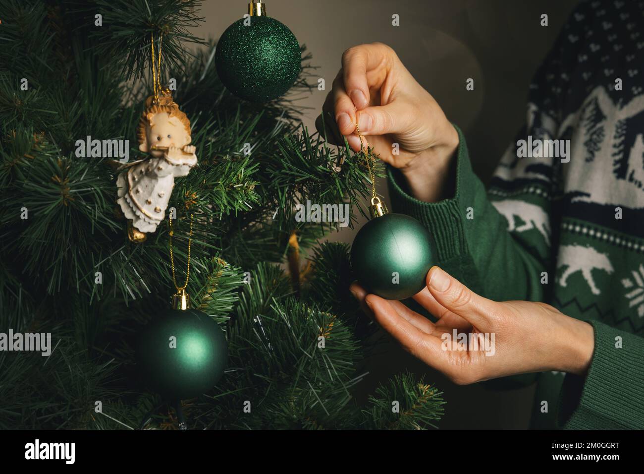 Einen weihnachtsbaum schmücken. Eine Nahaufnahme weiblicher Hände hängt einen grünen Ball an einen Ast Stockfoto
