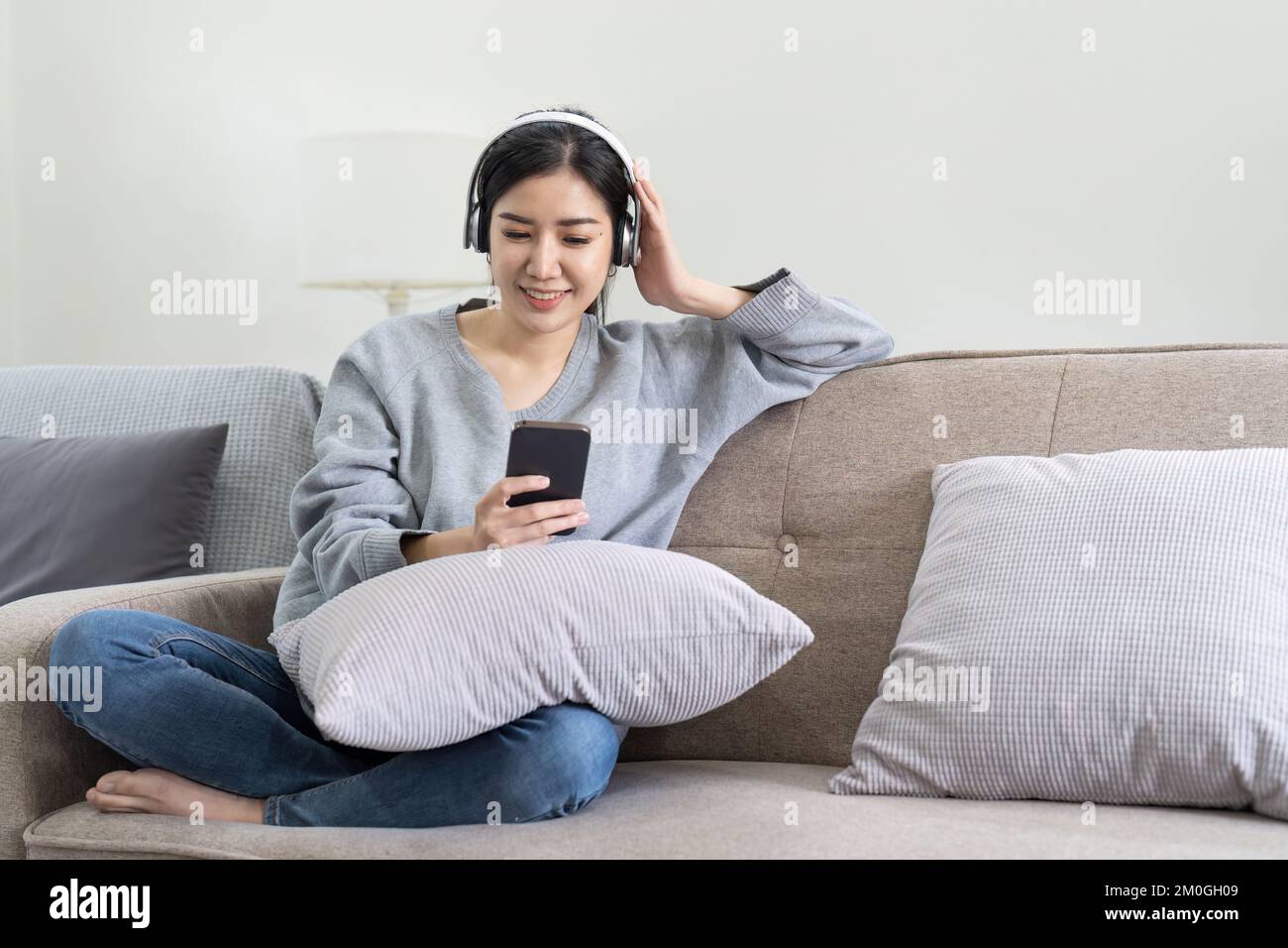 Asiatische Frauen hören Musik mit Mobiltelefon und Kopfhörern. Ein ruhiges Wochenende zu Hause, entspannen Sie sich auf dem Sofa, genießen Sie Ihre Lieblingsmusik, beliebte Musik, nutzen Sie modern Stockfoto