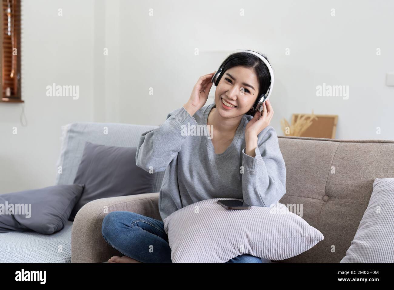 Asiatische Frauen hören Musik mit Mobiltelefon und Kopfhörern. Ein ruhiges Wochenende zu Hause, entspannen Sie sich auf dem Sofa, genießen Sie Ihre Lieblingsmusik, beliebte Musik, nutzen Sie modern Stockfoto