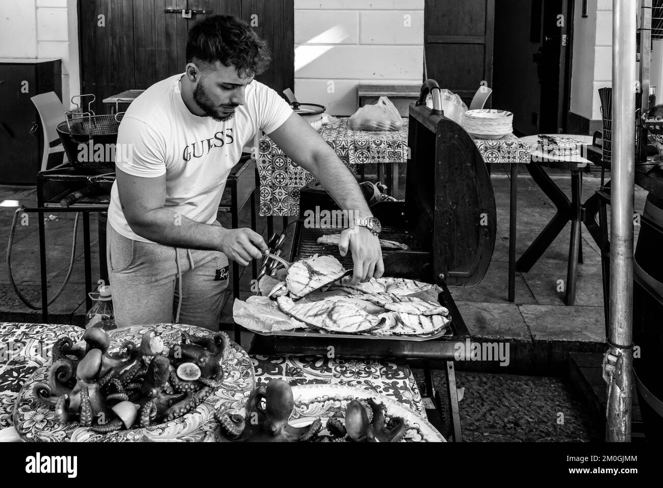 Ein junger Mann kocht Fisch auf Einem Grill auf dem Ballaro Street Market, Palermo, Sizilien, Italien. Stockfoto