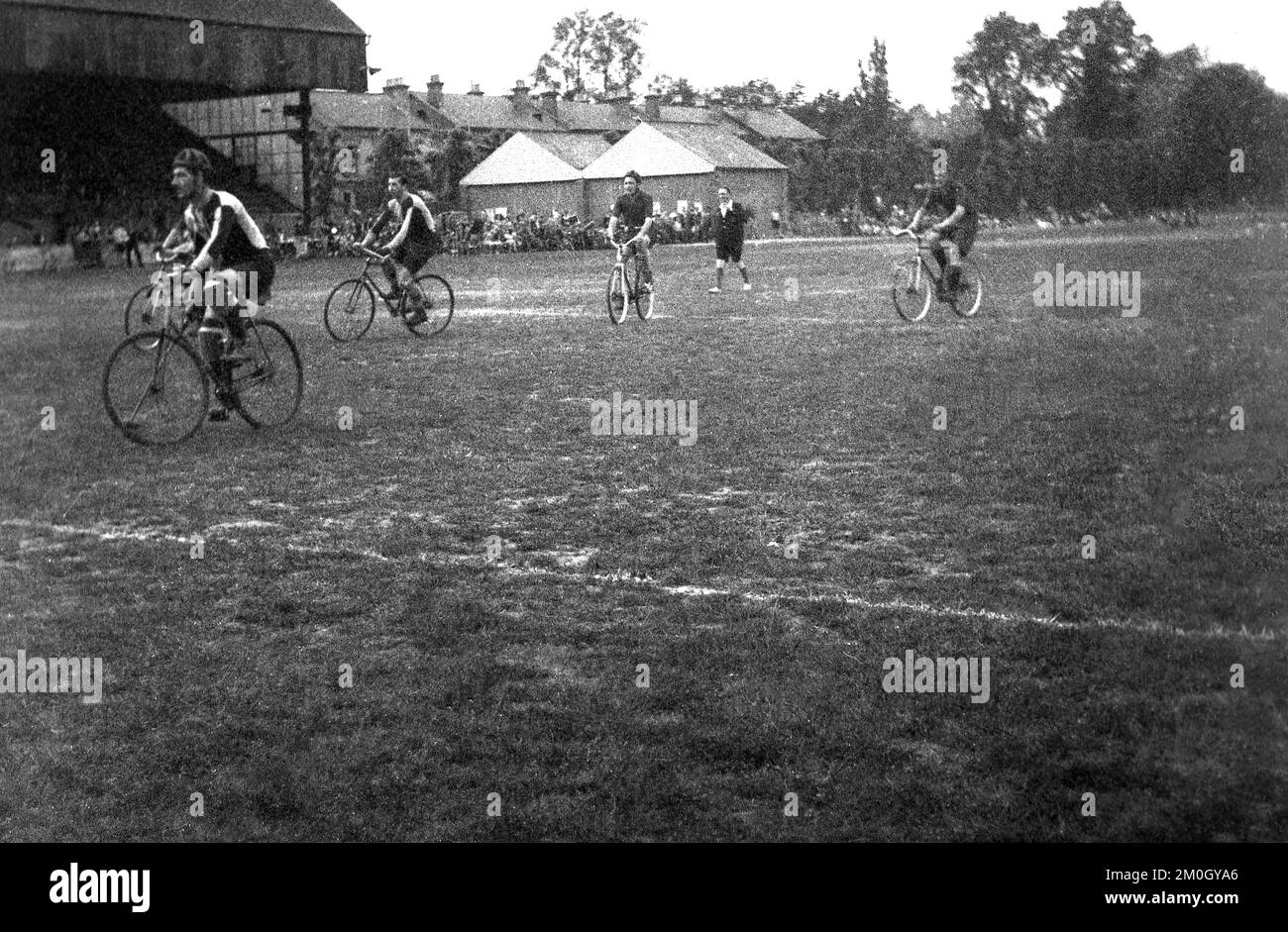 Etwa 1930er, historisch, ein Fahrrad-Polospiel, das draußen auf einem rauen, unebenen Rasenplatz gespielt wird, möglicherweise ein Fußballfeld, da es sich um eine heruntergekommene alte überdachte Haupttribüne in England, Großbritannien, handelt. Das Cycle Polo wurde 1891 in Irland in Co WIckow von Richard J. Mercredy, Herausgeber des Irish Cyclist Magazins, erfunden und war in den 1930er Jahren am beliebtesten. Stockfoto