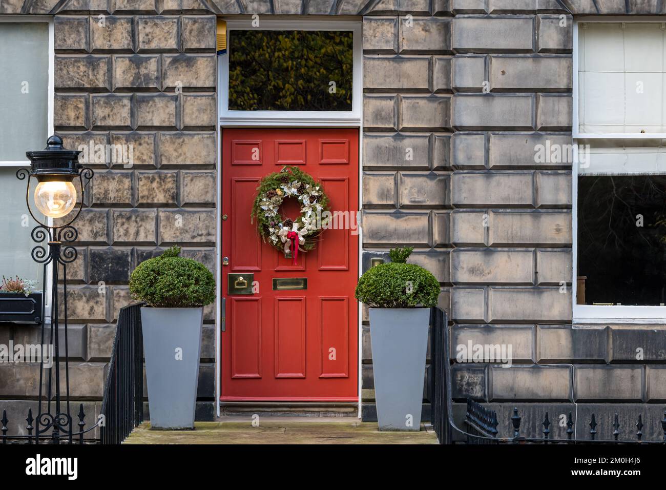 Edinburgh New Town, Schottland, Großbritannien, 6.. Dezember 2022. Kränze und Dekorationen der Weihnachtstüren: Die Bewohner der georgianischen Stadthäuser in der Neustadt sind bekannt für ihre prächtigen Dekorationen. Ein Weihnachtskranz an einer roten Haustür mit einer altmodischen Straßenlampe. Kredit: Sally Anderson/Alamy Live News Stockfoto