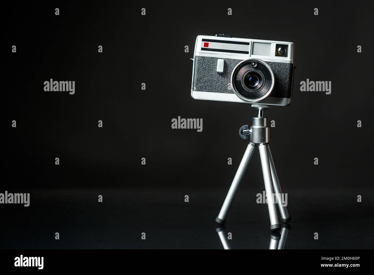 Oldtimer-60s-Fotokamera aus Metall auf Aluminium-Mini-Tripodon mit schwarzem Hintergrund. Analoges Kunst- und Fotografiekonzept. Stockfoto