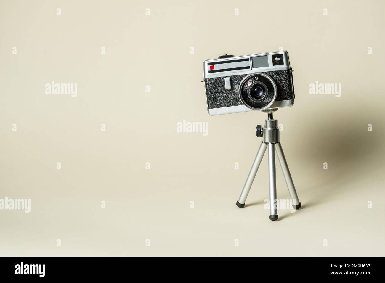 Klassische 60s-MP-Fotokamera aus Metall auf Aluminium-Mini-Tripodon mit beigefarbenem Hintergrund. Analoges Kunst- und Fotografiekonzept. Stockfoto