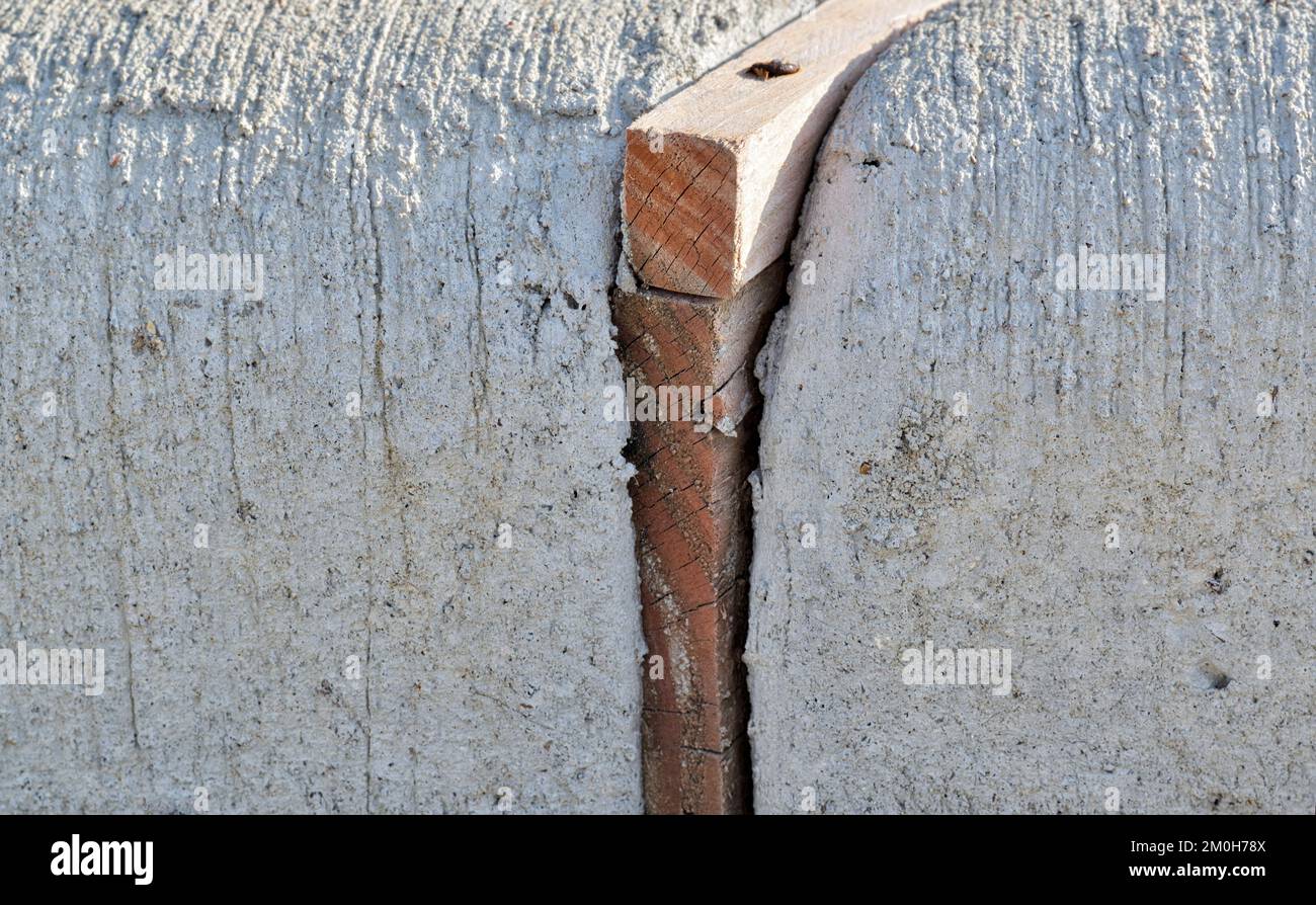 Spreizfugen aus Holz trennen Betonabschnitte einer Bordsteinkante, um Belastungen durch wärmebedingte Ausdehnung zu absorbieren. Nahaufnahme auf Bodenhöhe. Stockfoto