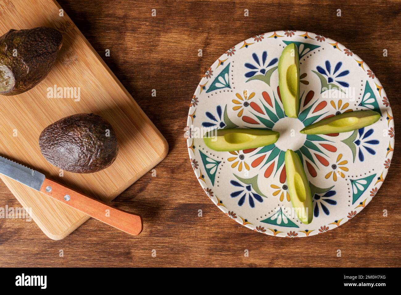 Avocado-Stücke auf einem rustikalen Teller auf einem Holztisch, begleitet von weiteren Avocados. Stockfoto