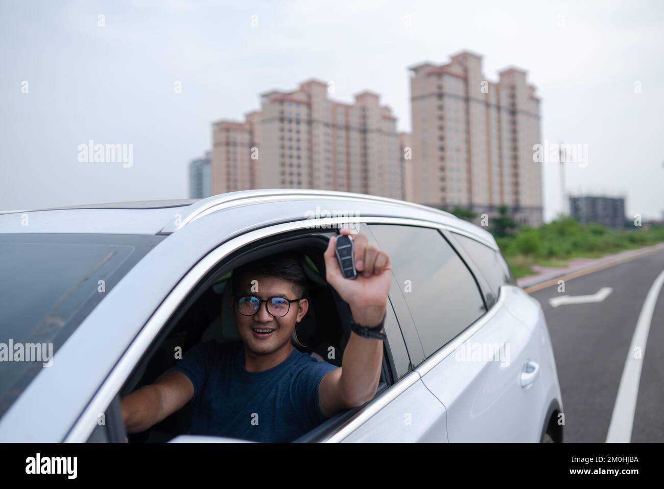 Der Asiate zeigt den Schlüssel eines innovativen Elektroautos Stockfoto