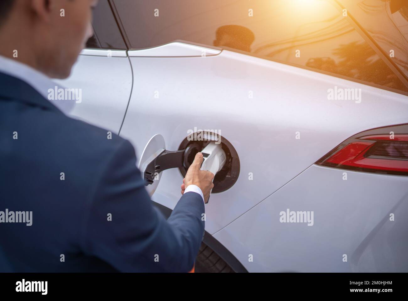 Ein junger Geschäftsmann lädt ein Elektrofahrzeug an einer Ladestation für Elektrofahrzeuge auf. Stockfoto