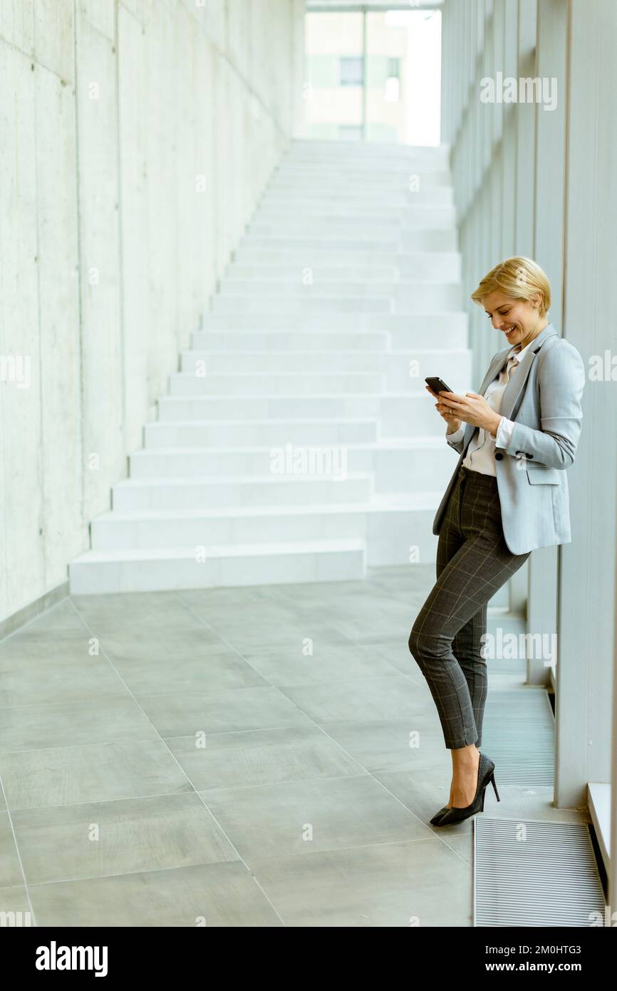 Geschäftsfrau, die auf dem modernen Büroflur mit dem Mobiltelefon steht Stockfoto
