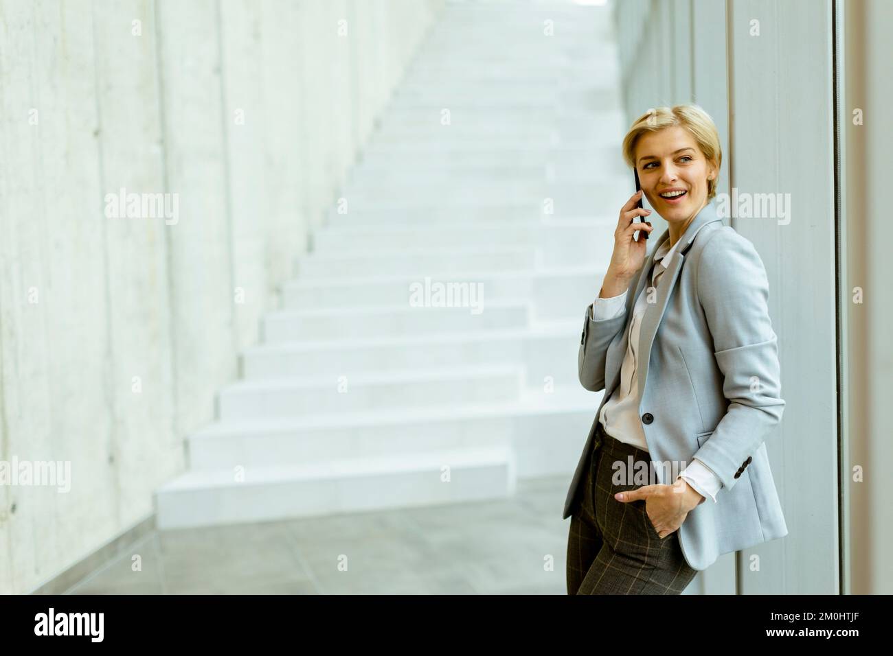 Geschäftsfrau, die auf dem modernen Büroflur mit dem Mobiltelefon steht Stockfoto
