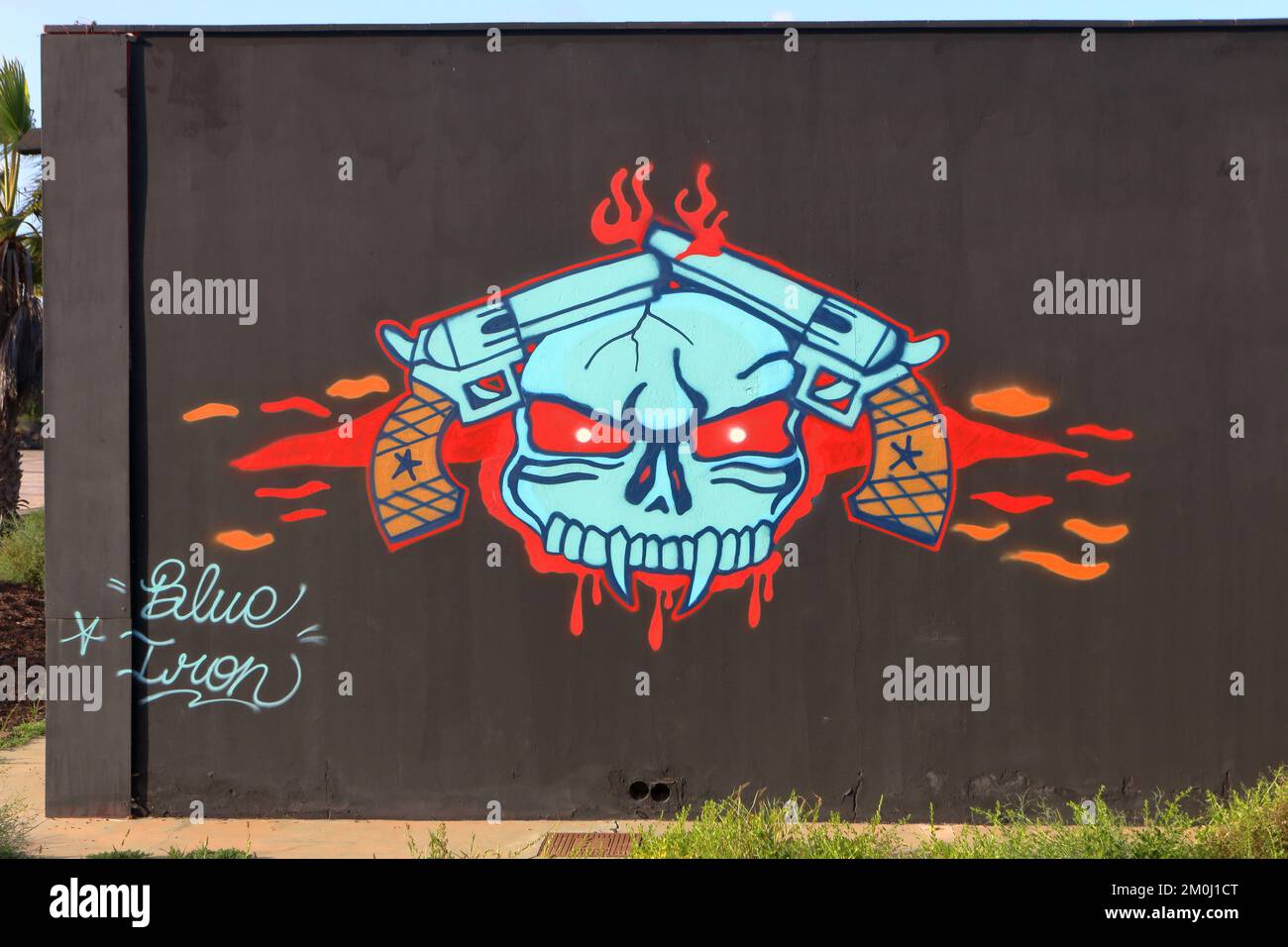 Graffiti-Kunst eines Schädels und 2 Waffen an einer schwarzen Wand Stockfoto