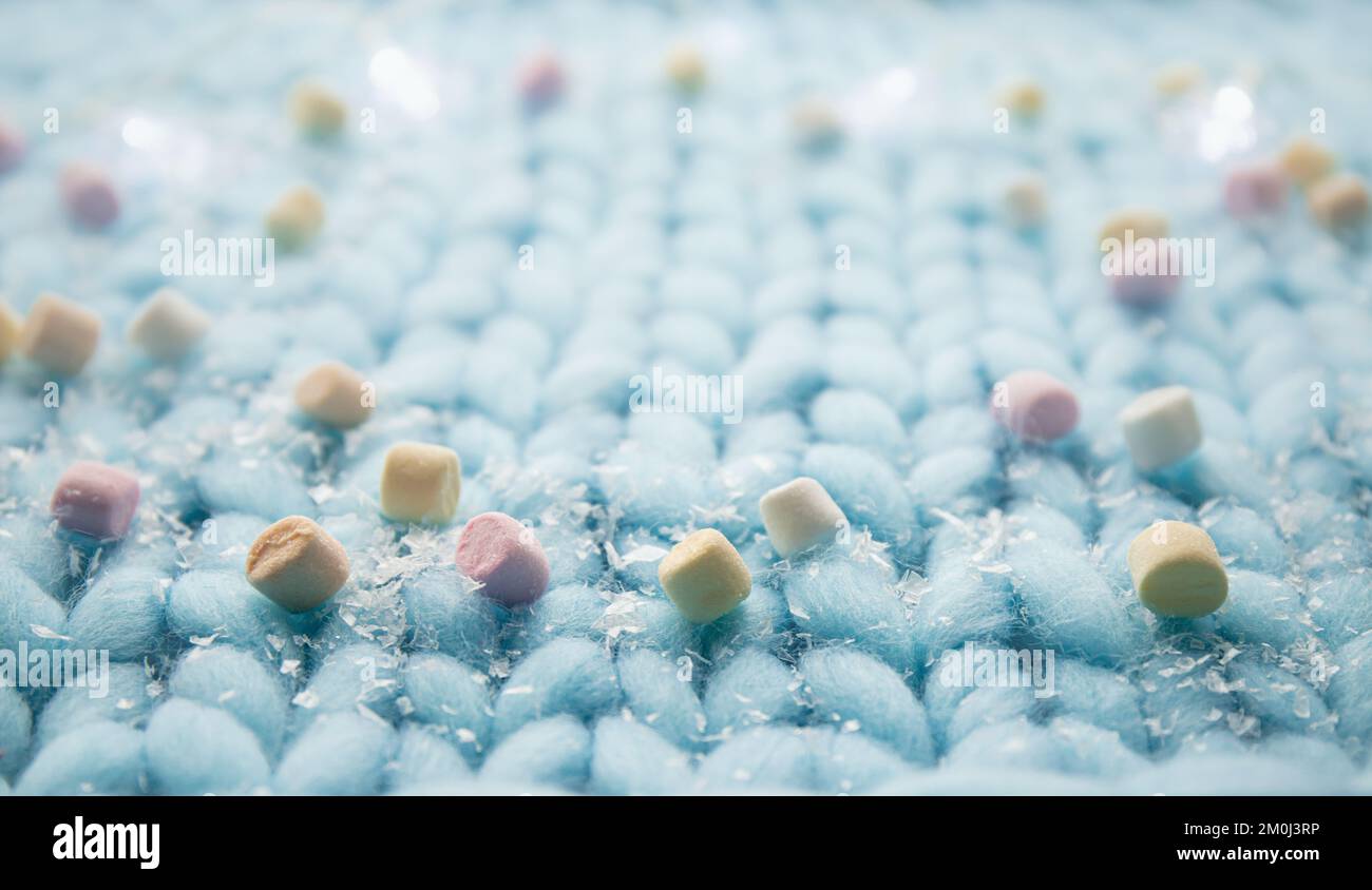 Seitenansicht: Hellblauer, weicher gestrickter Wollhintergrund mit Mini-Marshmallows, weihnachtlicher Winterrahmen mit Kopierbereich. Stockfoto