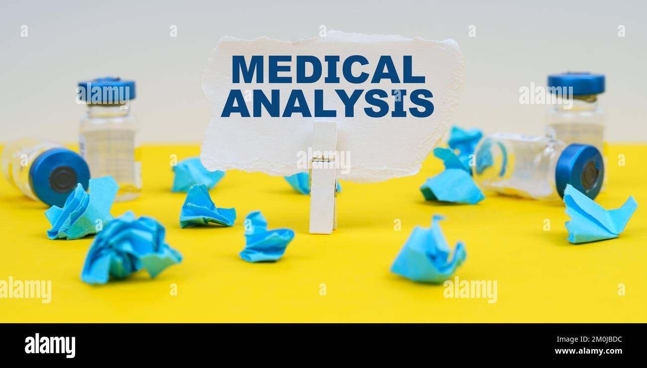 Medizin und Gesundheitskonzept. Auf gelbem Hintergrund befinden sich Ampullen, blau zerknittertes Papier und Papier mit der Aufschrift -MEDIZINISCHE ANALYSE Stockfoto