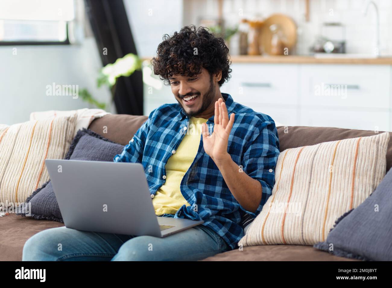 Ein indischer Mann, der sich auf dem Sofa entspannt und per Videoanruf mit Freunden zu Hause online chattet Stockfoto